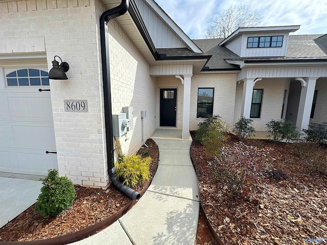 doorway to property featuring brick siding, roof with shingles, and an attached garage