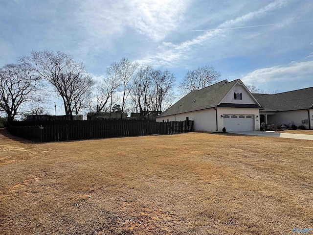 view of yard featuring an attached garage, fence, and concrete driveway