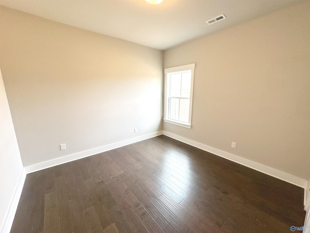 spare room featuring dark wood-style flooring, visible vents, and baseboards