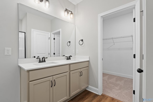 full bath with a walk in closet, double vanity, wood finished floors, and a sink