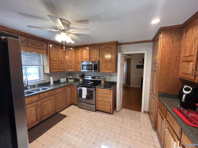 kitchen featuring sink, ceiling fan, appliances with stainless steel finishes, ornamental molding, and a textured ceiling