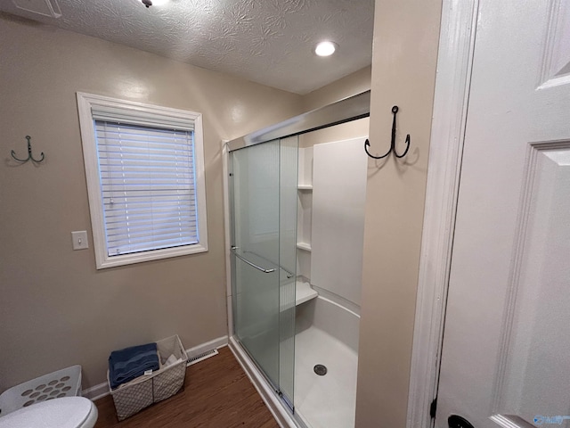 bathroom with hardwood / wood-style floors, a shower with shower door, toilet, and a textured ceiling