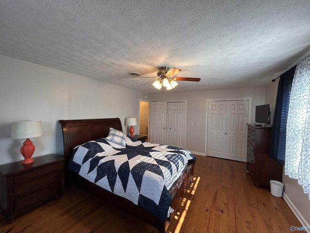 bedroom with dark hardwood / wood-style floors, two closets, a textured ceiling, and ceiling fan