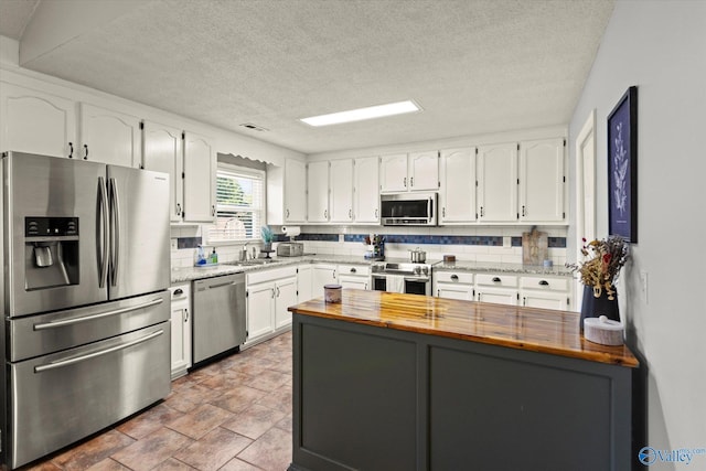 kitchen featuring butcher block countertops, white cabinetry, stainless steel appliances, and a textured ceiling