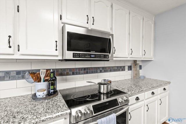 kitchen featuring decorative backsplash, light stone countertops, white cabinetry, and stainless steel appliances