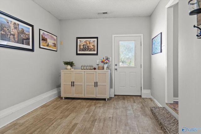 doorway to outside featuring a textured ceiling and light hardwood / wood-style flooring