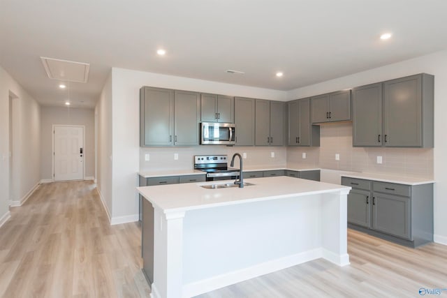 kitchen with light hardwood / wood-style floors, stainless steel appliances, gray cabinets, and an island with sink