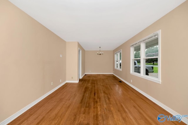 spare room with an inviting chandelier and wood-type flooring