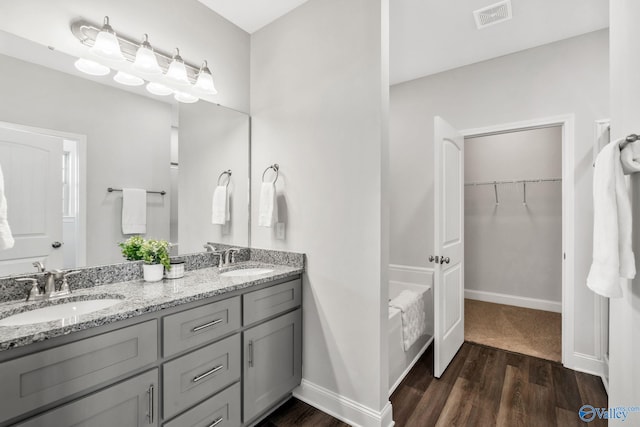 full bathroom featuring a spacious closet, visible vents, a sink, and wood finished floors