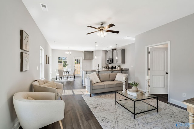 living room featuring ceiling fan with notable chandelier, wood finished floors, visible vents, and baseboards