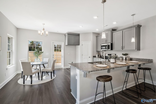 kitchen featuring dark wood-style floors, stainless steel microwave, light stone counters, gray cabinetry, and a sink