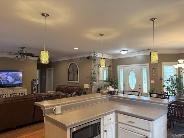 kitchen with stainless steel microwave, decorative light fixtures, open floor plan, a ceiling fan, and white cabinets
