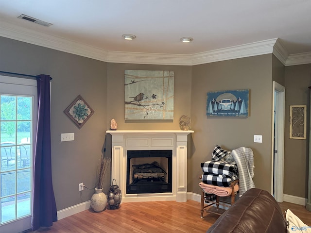 living area with wood finished floors, a fireplace, crown molding, visible vents, and baseboards