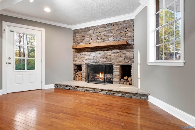 unfurnished living room with wood-type flooring, a textured ceiling, a stone fireplace, and crown molding