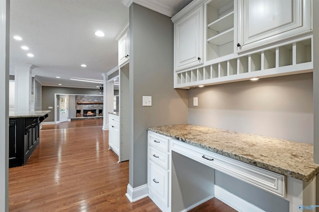 kitchen with light stone counters, white cabinets, wood-type flooring, and ornamental molding