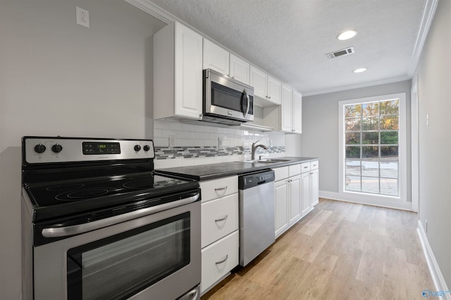 kitchen featuring white cabinetry, sink, light wood-type flooring, appliances with stainless steel finishes, and ornamental molding