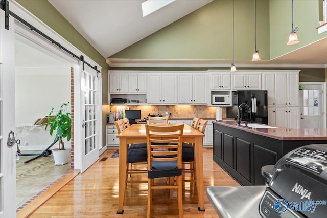 kitchen with white microwave, freestanding refrigerator, pendant lighting, white cabinetry, and a barn door