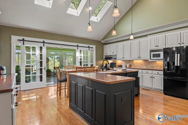 kitchen with white cabinetry, black appliances, light wood-style flooring, and a barn door
