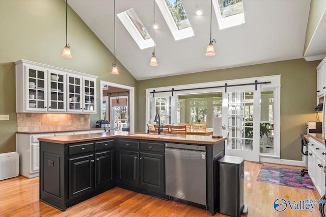 kitchen with light wood-type flooring, a sink, stainless steel dishwasher, white cabinetry, and dark cabinets