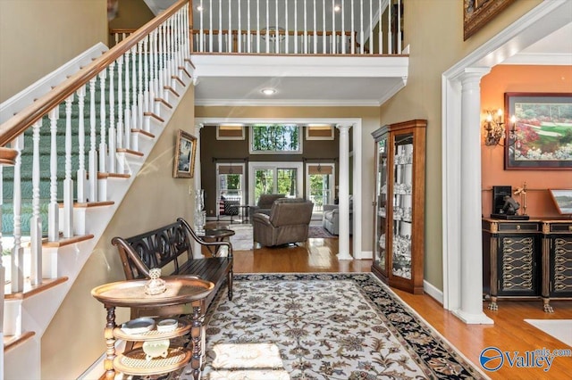entrance foyer with a towering ceiling, ornamental molding, ornate columns, and wood finished floors
