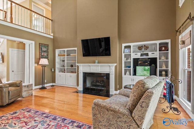 living room featuring a fireplace with flush hearth, wood finished floors, baseboards, and a towering ceiling