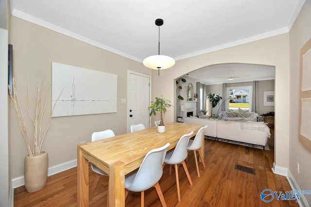 dining space with arched walkways, crown molding, and wood finished floors