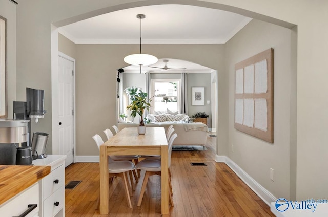 dining space with visible vents, arched walkways, light wood-type flooring, baseboards, and ceiling fan