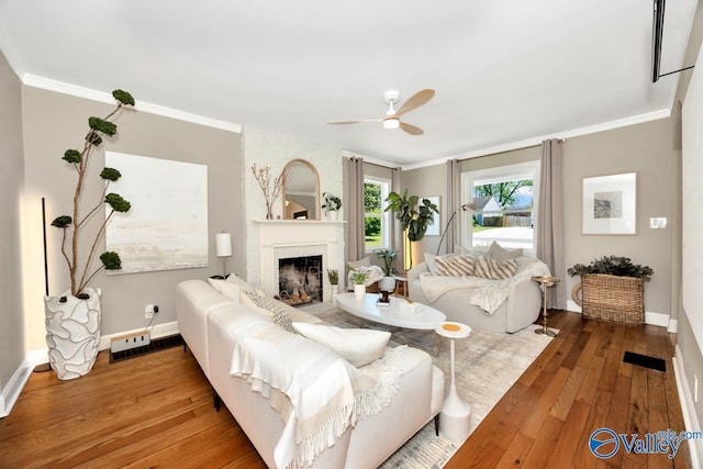 living area with baseboards, ceiling fan, crown molding, hardwood / wood-style floors, and a fireplace