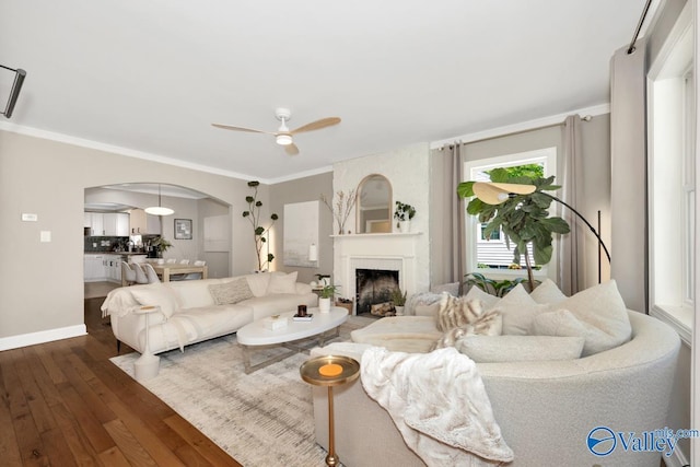 living area featuring arched walkways, crown molding, a ceiling fan, and dark wood-style flooring