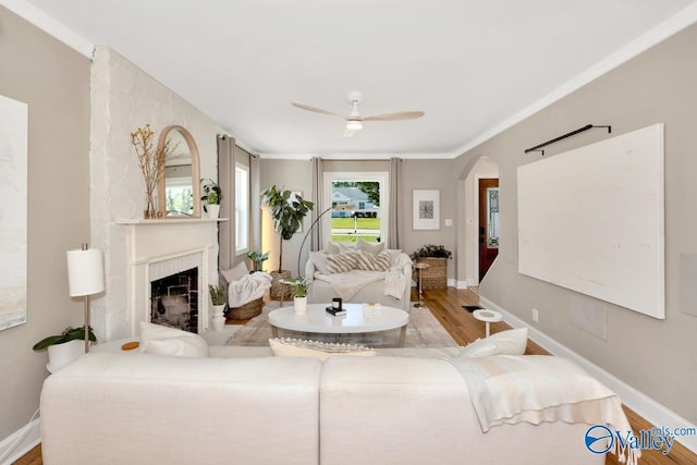 living room featuring wood finished floors, arched walkways, baseboards, a fireplace, and ceiling fan