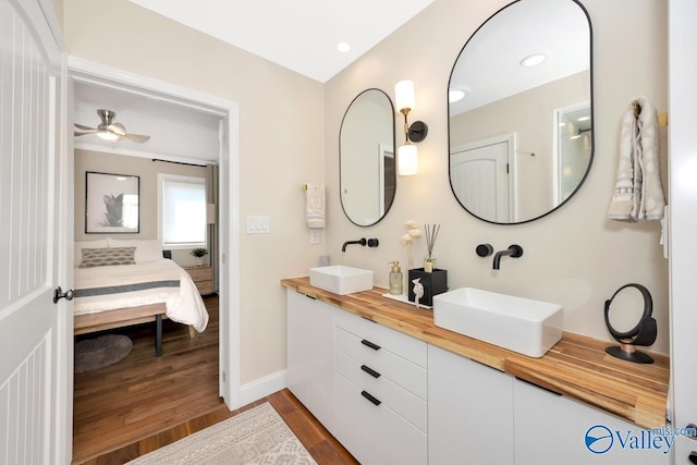 ensuite bathroom featuring wood finished floors, a sink, double vanity, and connected bathroom