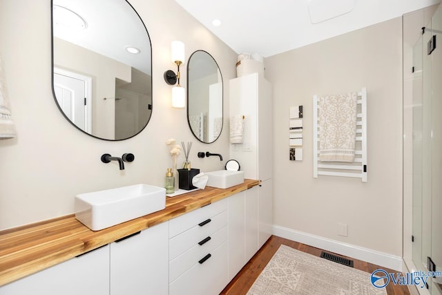 bathroom featuring baseboards, wood finished floors, a sink, and visible vents