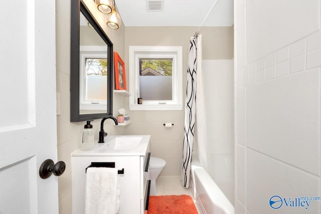 bathroom featuring vanity, shower / bathtub combination with curtain, tile walls, toilet, and visible vents
