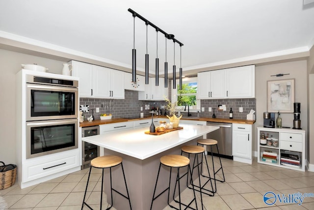 kitchen with a kitchen bar, appliances with stainless steel finishes, beverage cooler, and light tile patterned flooring