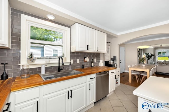 kitchen featuring stainless steel dishwasher, a sink, butcher block countertops, decorative backsplash, and ornamental molding