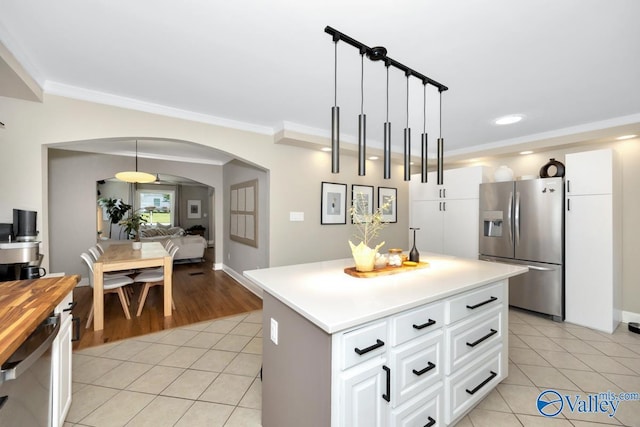 kitchen featuring a center island, crown molding, light tile patterned floors, arched walkways, and appliances with stainless steel finishes