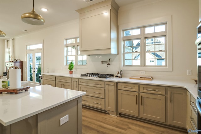 kitchen with light wood-type flooring, stainless steel gas cooktop, ornamental molding, decorative light fixtures, and tasteful backsplash