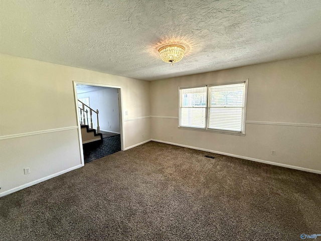 spare room featuring dark carpet, a textured ceiling, baseboards, and visible vents
