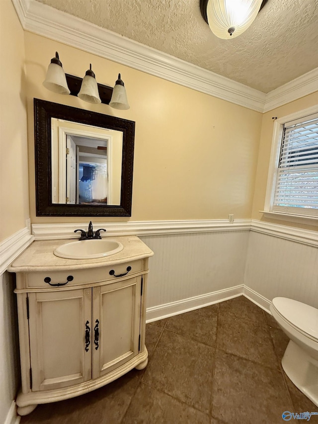 half bath with ornamental molding, toilet, wainscoting, vanity, and tile patterned floors