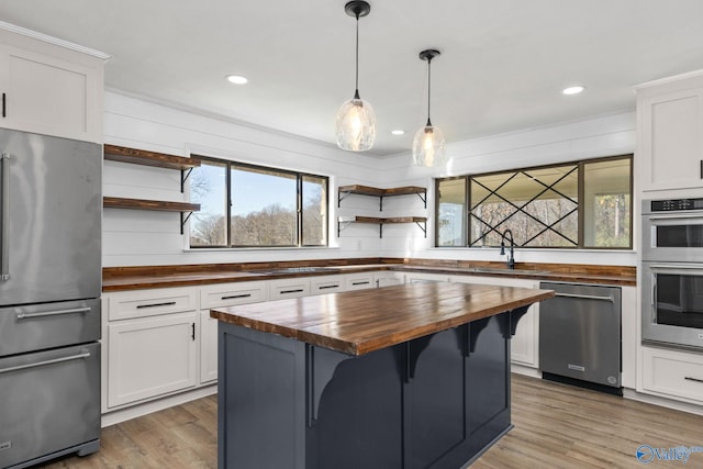 kitchen featuring a kitchen bar, appliances with stainless steel finishes, sink, white cabinetry, and butcher block counters