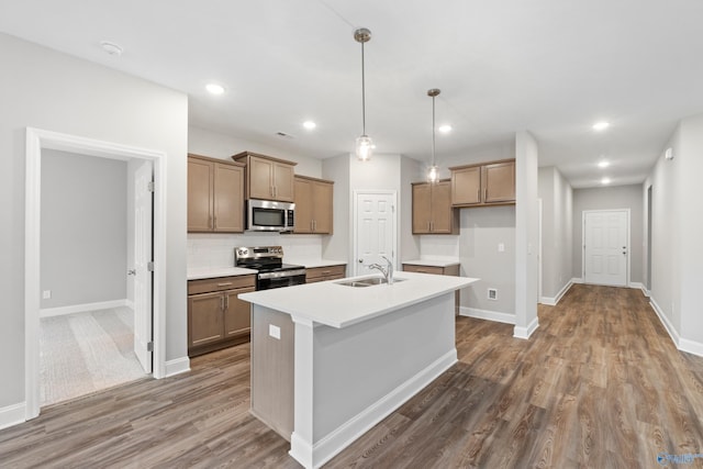 kitchen featuring hardwood / wood-style floors, tasteful backsplash, hanging light fixtures, stainless steel appliances, and a center island with sink