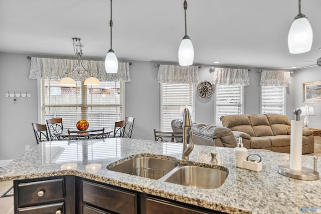 kitchen featuring dark brown cabinets, light stone countertops, sink, and hanging light fixtures