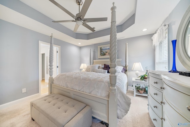 bedroom featuring ceiling fan, light colored carpet, and a tray ceiling