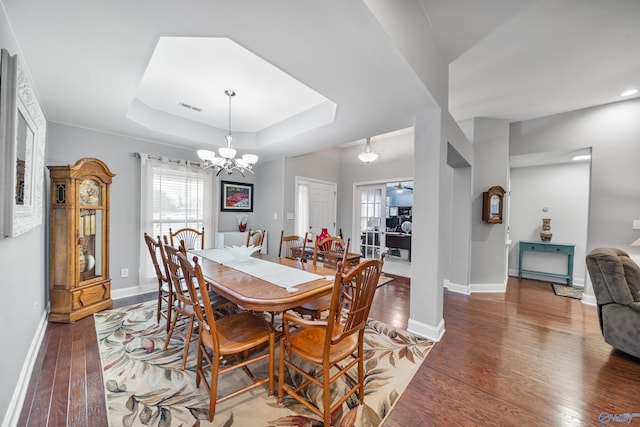 dining space with hardwood / wood-style flooring, a tray ceiling, and a chandelier