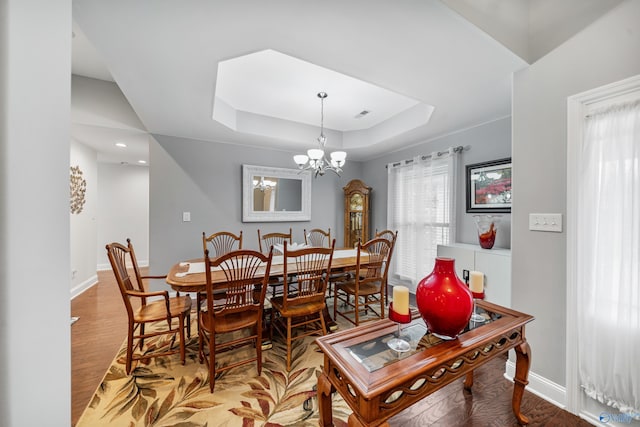 dining area featuring a raised ceiling, wood-type flooring, and an inviting chandelier