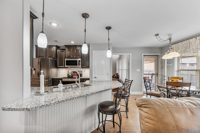 kitchen with sink, dark brown cabinets, stainless steel appliances, tasteful backsplash, and light tile patterned flooring