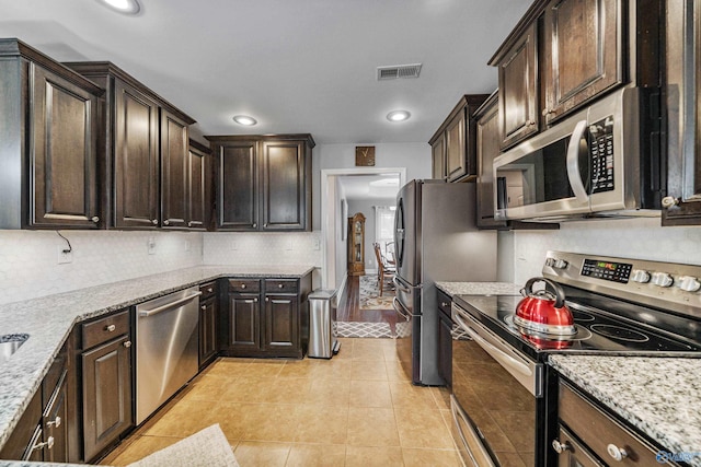 kitchen featuring appliances with stainless steel finishes, light tile patterned floors, dark brown cabinetry, and decorative backsplash