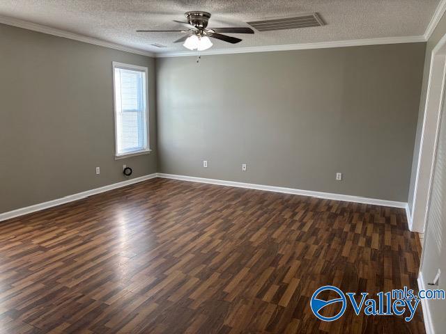 empty room with ornamental molding, a textured ceiling, and dark wood-type flooring