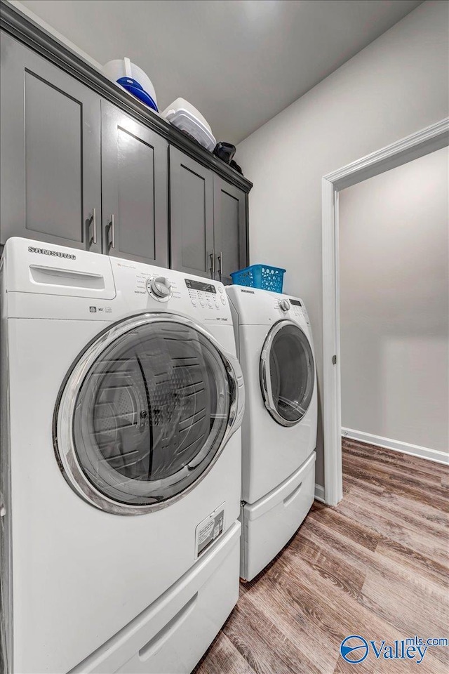 clothes washing area featuring washer and dryer, cabinets, and hardwood / wood-style flooring