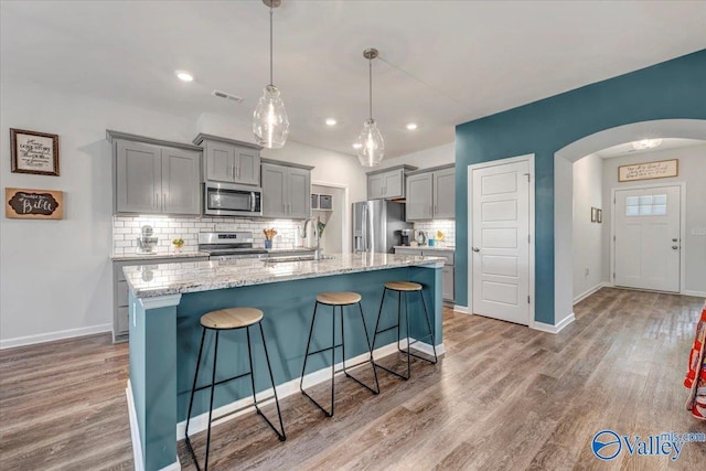 kitchen with decorative light fixtures, stainless steel appliances, a kitchen breakfast bar, backsplash, and a kitchen island with sink